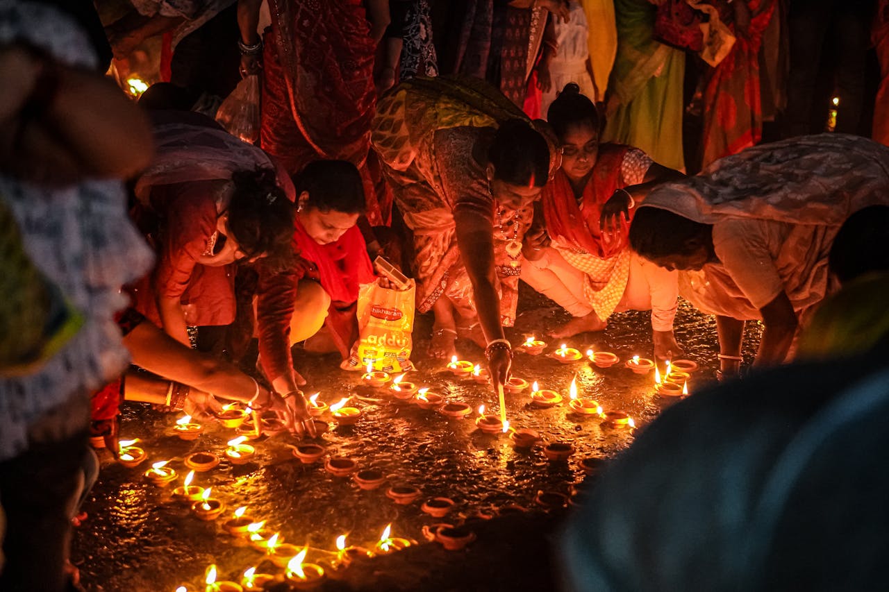 People lighting traditional oil lamps during a nighttime festival celebration.